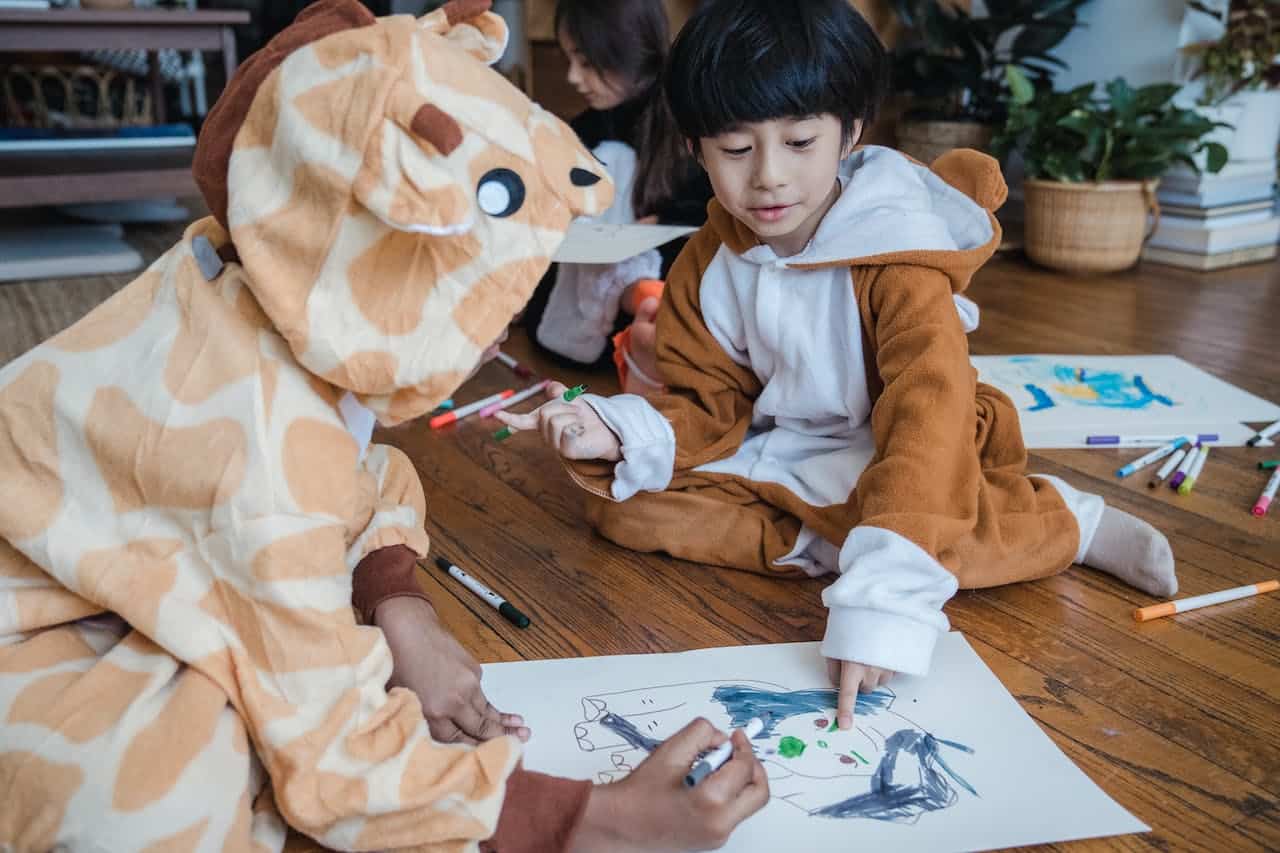 Copii acasa. copii îmbrăcați în pijamăluțe animale, desenează stând pe jos
